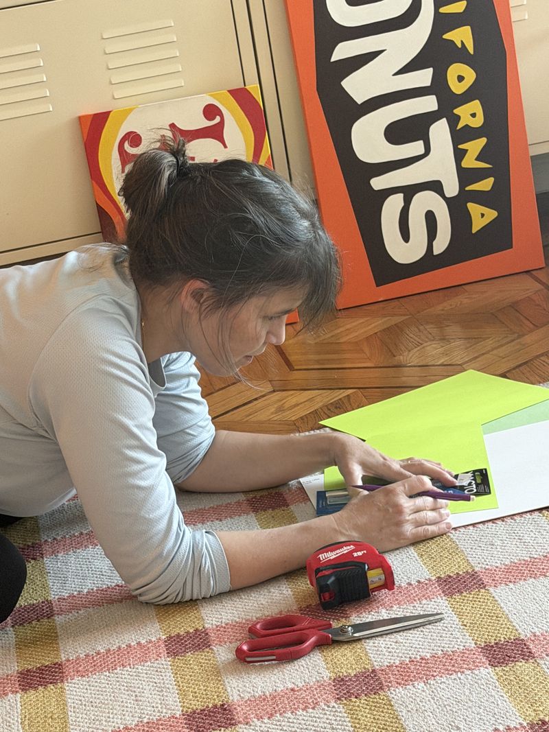 An artist lying on the floor cutting out a sign by hand, on Justin Michael's project